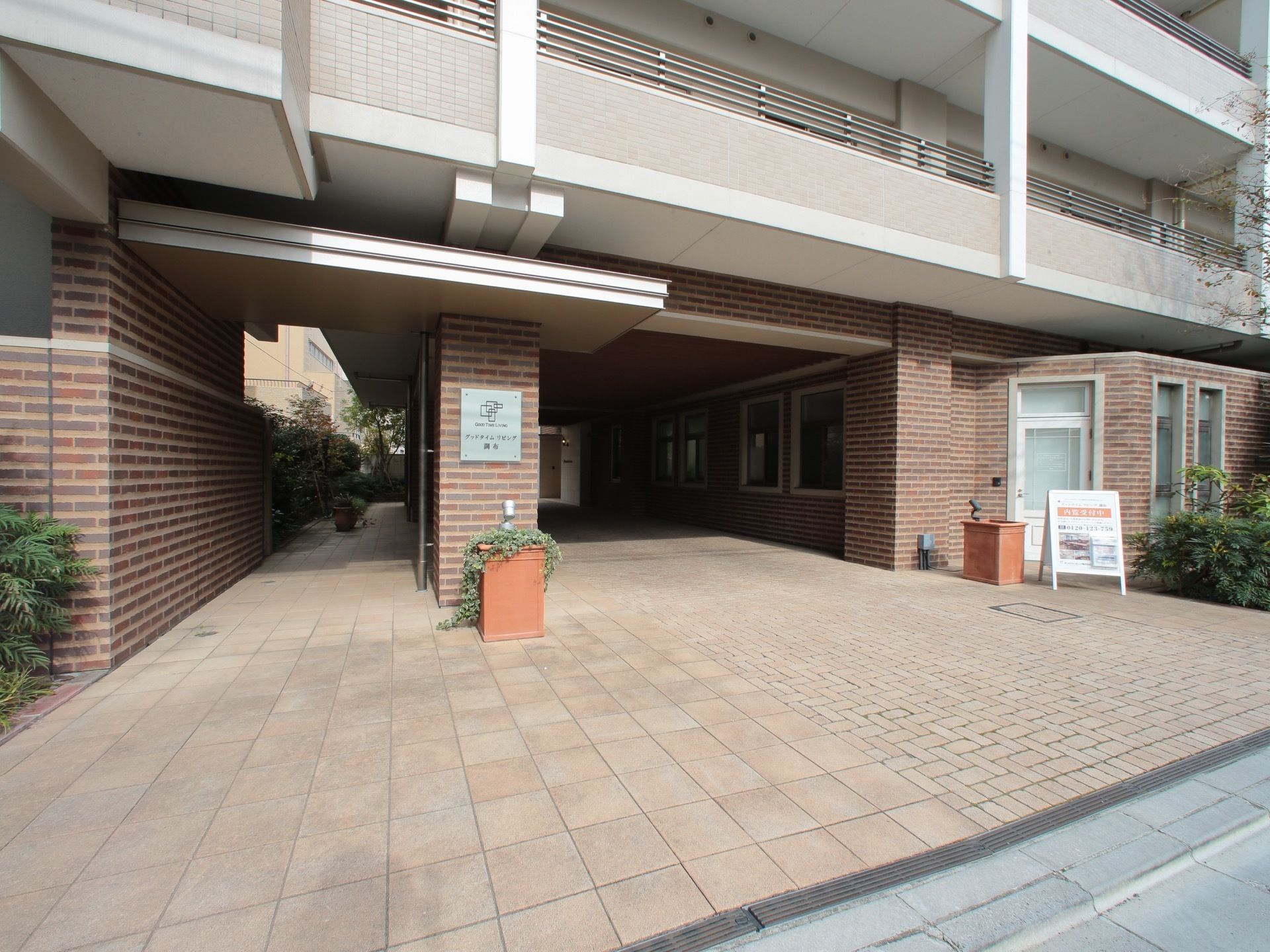 １階部分には、空洞を設け、入口の外壁には、表札を掲げている。上階は、白色系のタイル調の外観である。建物傍は、緑豊かである。