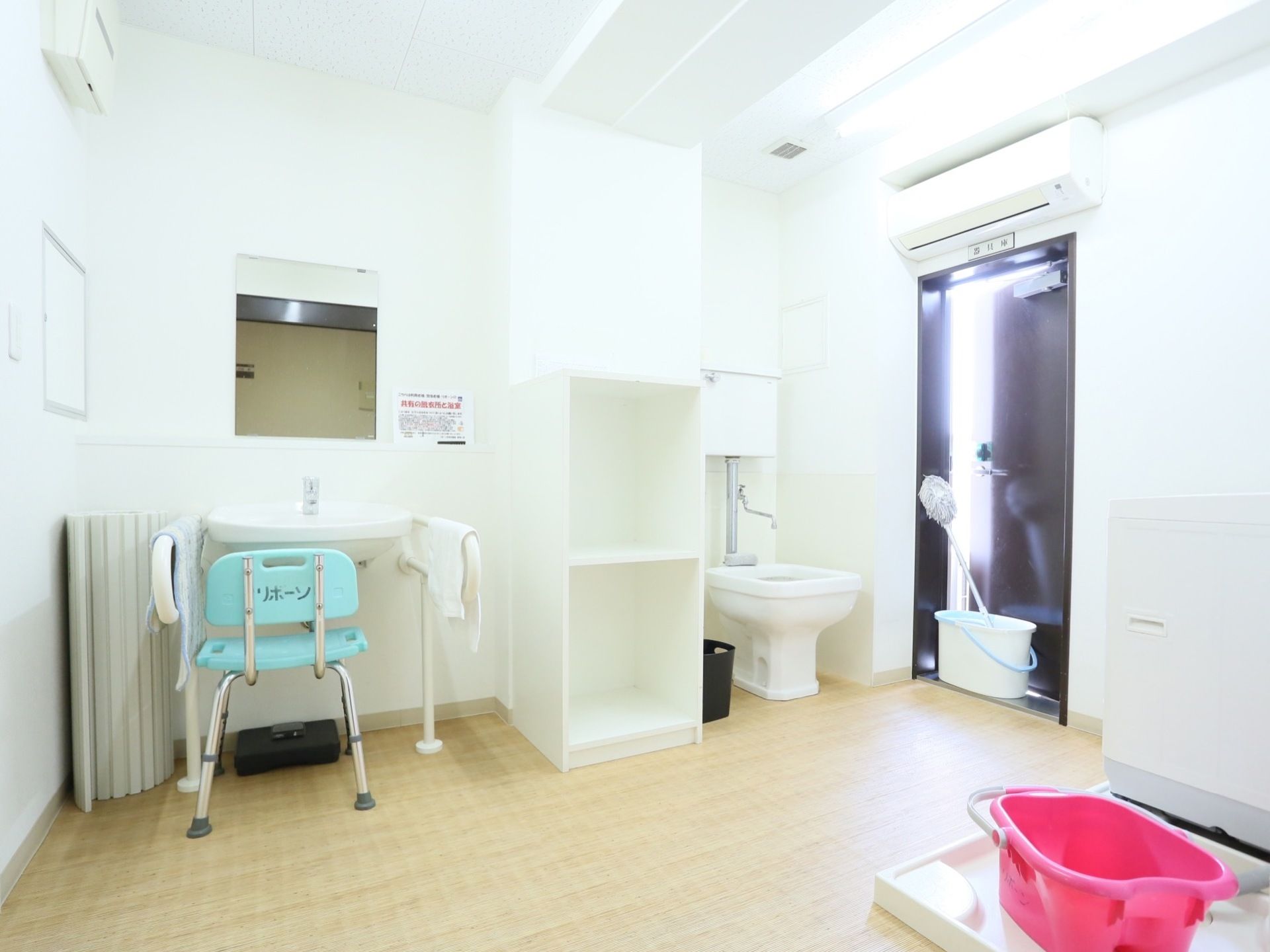 洗面台や流し、洗濯機などが置かれた部屋がある。白色を基調としたきれいな空間である。勝手口の上にエアコンが設置されている。