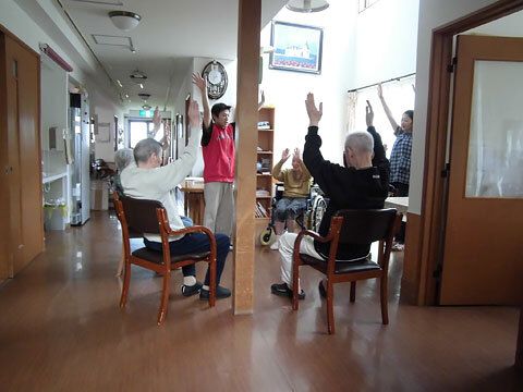 共有スペースで体操をしている入居者たち。輪の中央には男性スタッフがいて、手本を見せている。