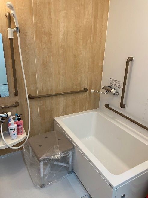 赤い手すりが設置されたモノトーンの浴室にはシャワーが2か所に設置され、シャワーチェアもある。