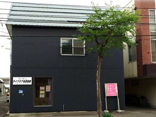バス停から徒歩１分の場所にある紺色の壁の２階建ての建物である。アクセスがよく、ご家族にお気軽に来訪していただける。