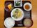 白いご飯に味噌汁、天ぷらの盛り合わせに野菜の和え物、フルーツの盛り合わせなどが並んだ黒いトレー。