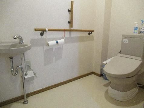 縦横に手すりが設置されたトイレは広く、手洗い場も付いている。便座の後ろにはスプレーのようなものがある。