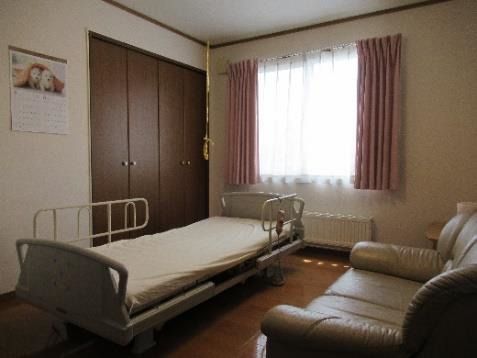 大きなソファやベッドが置かれたフローリングの部屋にはレースカーテンとカーテンが付いた窓がある。