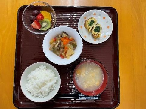 煮物や具入りの卵焼き、白いご飯に味噌汁、カットフルーツの盛り合わせなどが並んだトレー。