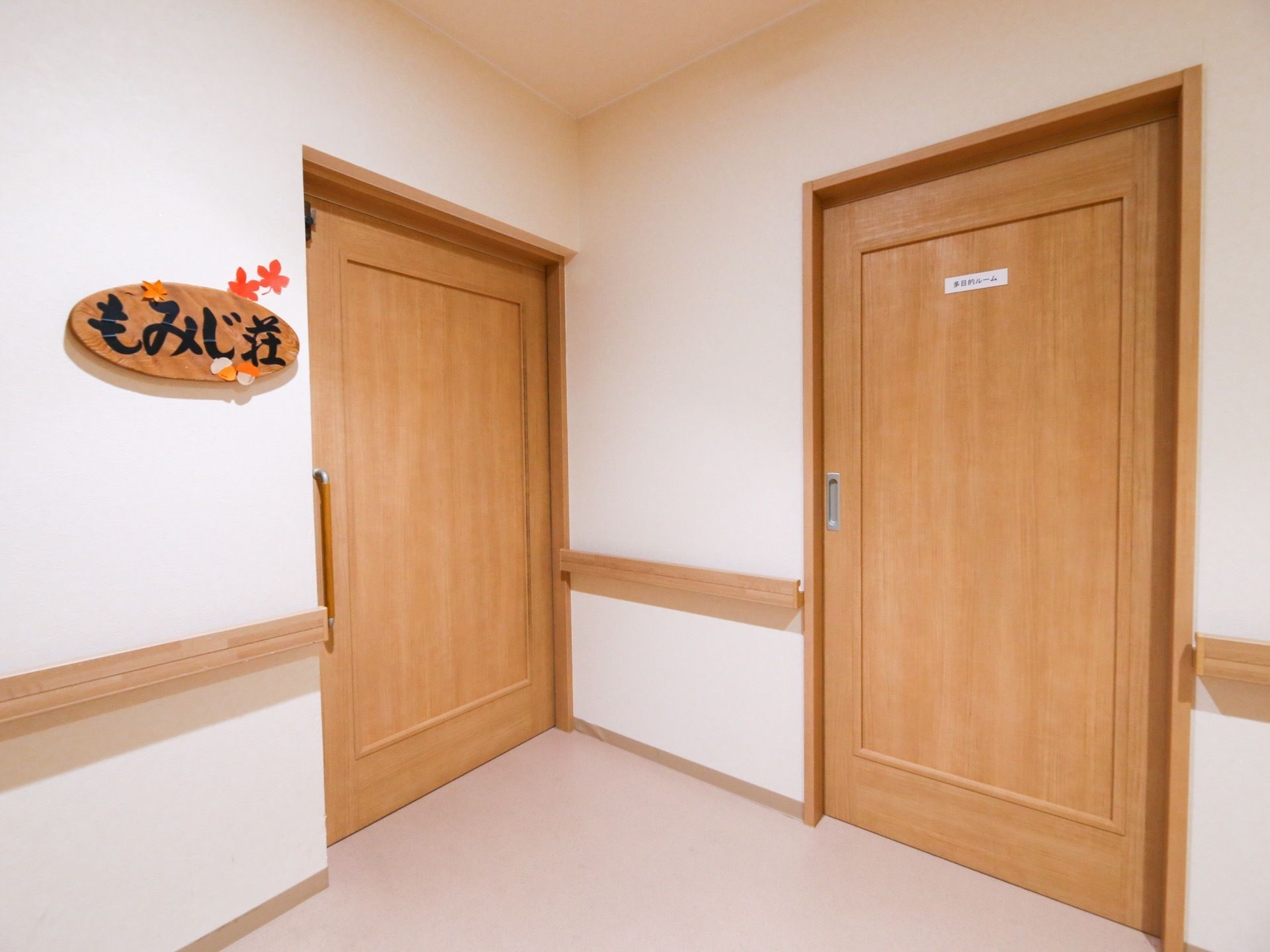 白い壁紙の廊下で、手すりや居室のドアが木製である。大きな引き戸のドアで、開閉しやすい。もみじ荘と書かれたプレートが飾ってある。