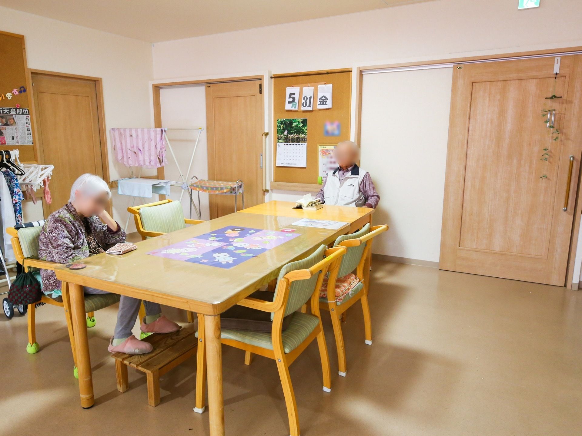居室の前にリビングがあり、テーブルと椅子が用意されている。壁にはコルクボードが貼ってあり、日付と曜日が展示されている。