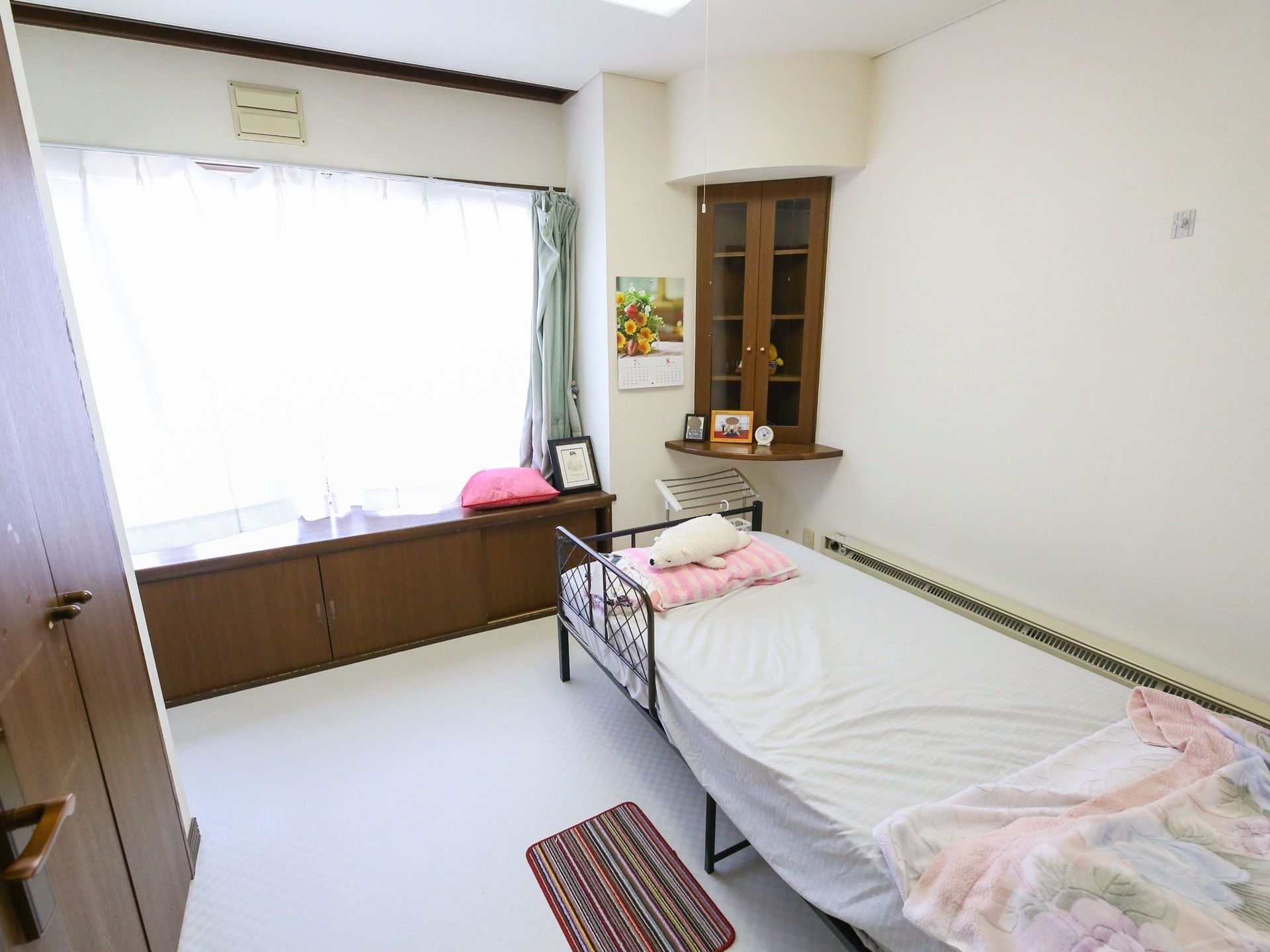 壁と床を白で統一した居室である。右手にベッドがあり、布団が敷かれている。左手と窓の下に収納スペースがある。