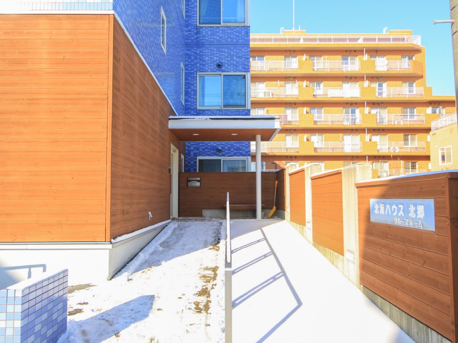 玄関前に傾斜が緩やかなスロープが設置されており、木製の塀には施設名が書かれた表札が付けられている