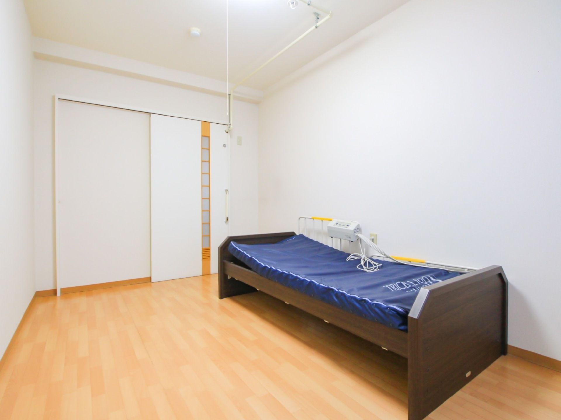 スプリンクラーが完備されているワンルームの居室。壁には介護ベッドが設置されており、リモコンや柵が付けられている