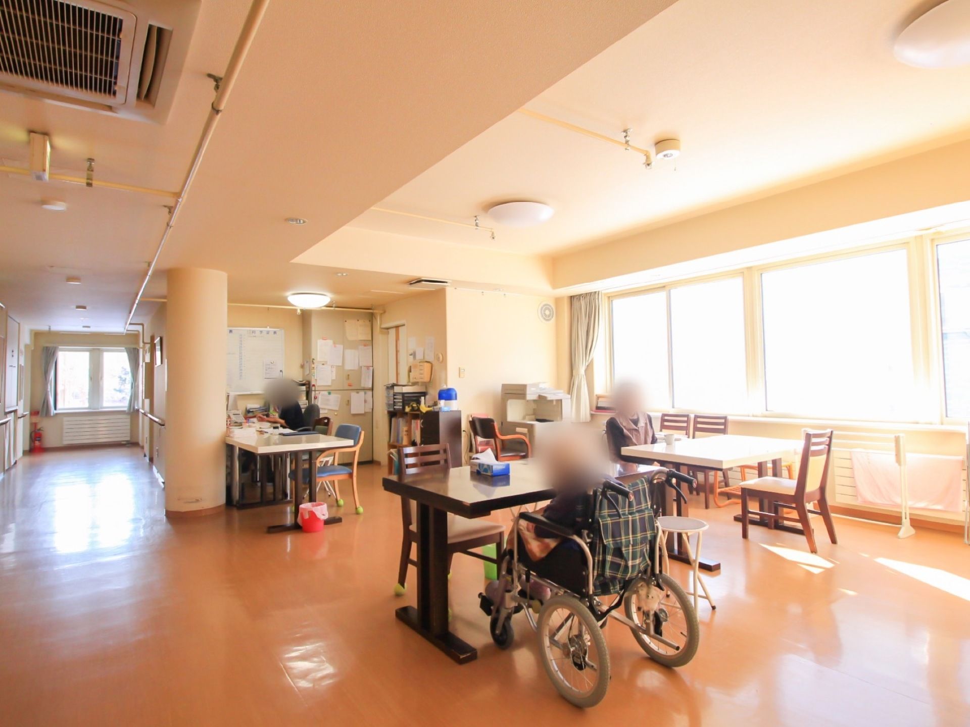 通路途中に設けられている開放的なリビングで入居者様が寛いでいる。フロアの一角に、スタッフのスペースが確保されている。