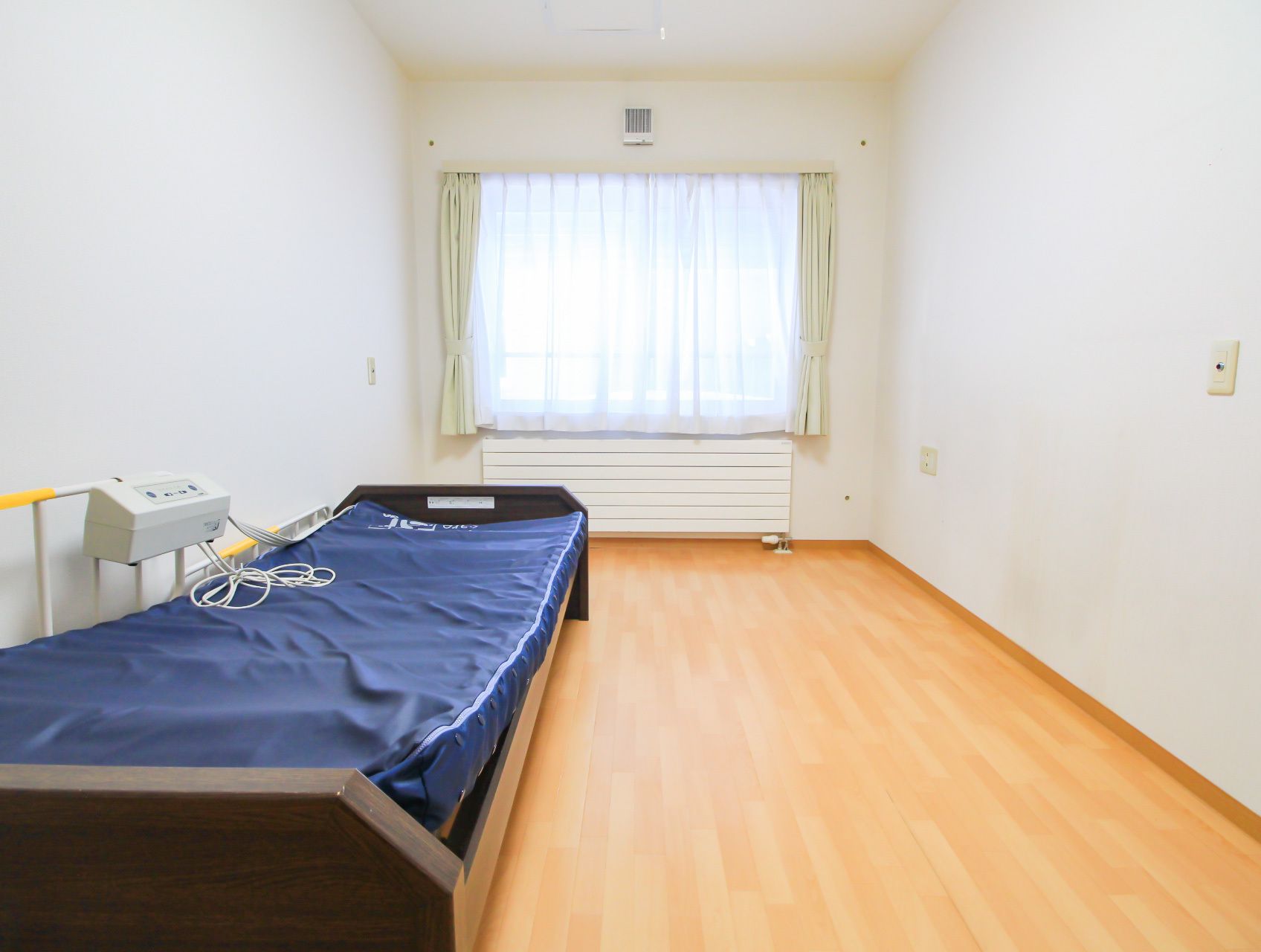 天井と壁が白く明るい、介護用のベッドが置かれている居室