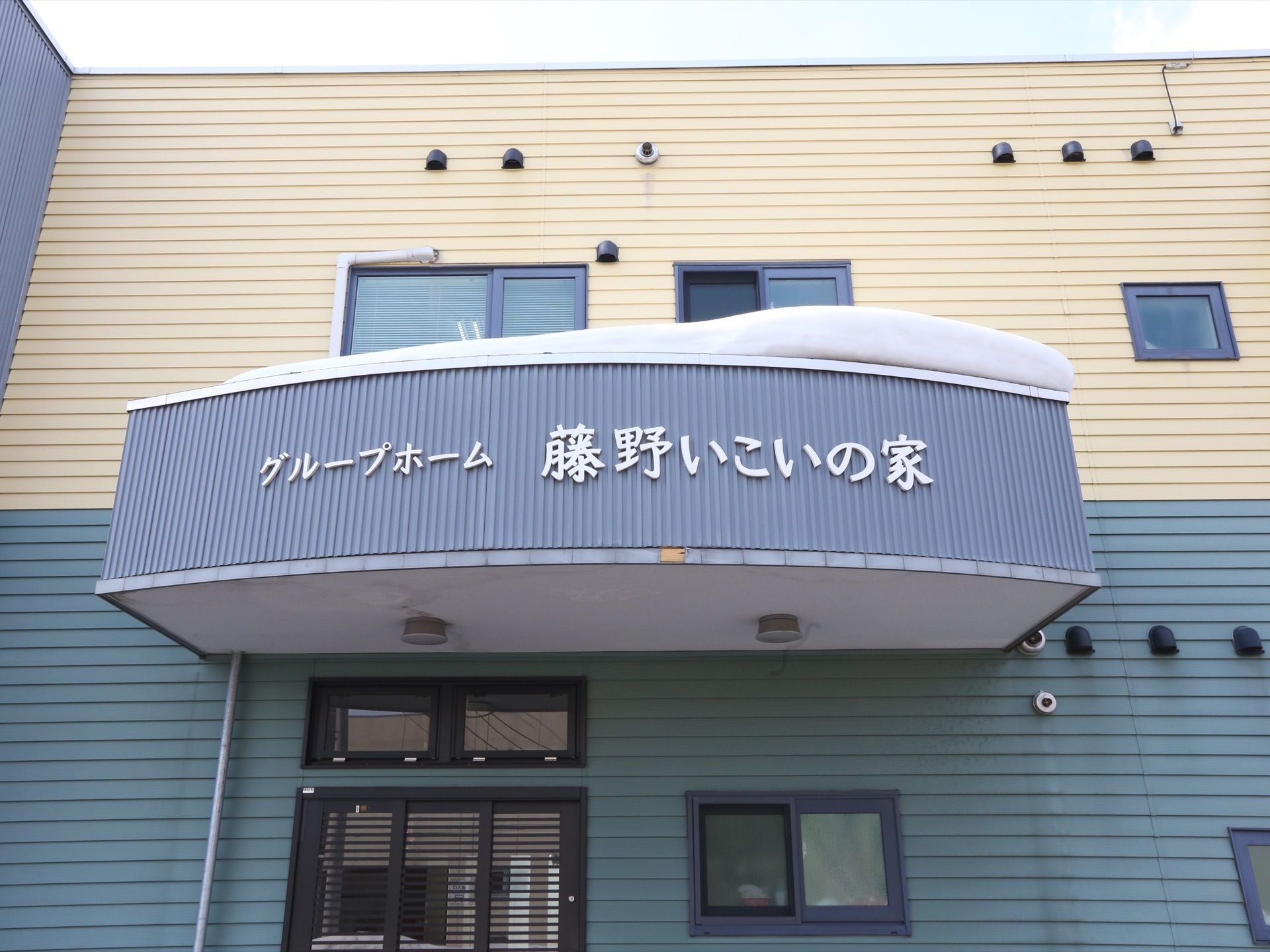 エントランスには大きなひさしが設置されており、正面に施設名が記されている。玄関扉には、引きドアが採用されている。