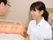 髪を一つに結んだ女性スタッフが笑顔で眼鏡をかけた高齢男性と話している。