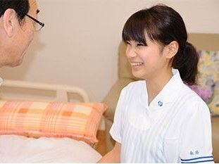 髪を結んだ若い女性スタッフが笑顔で眼鏡をかけた高齢男性と話している。