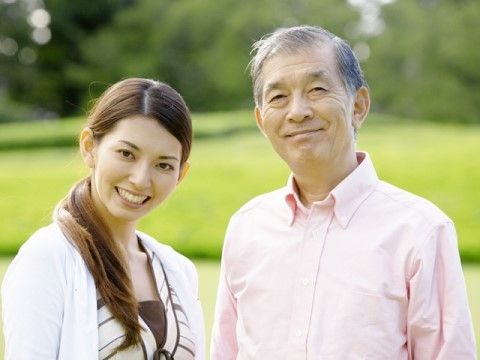 緑広がる公園でこちらを向いて微笑んでいる若い人と高齢者。孫と祖父、スタッフと高齢者