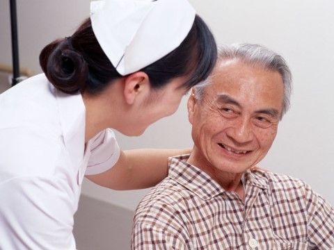 看護師が高齢者に何かを話しかけている様子。お互いに目を見て微笑んでいる