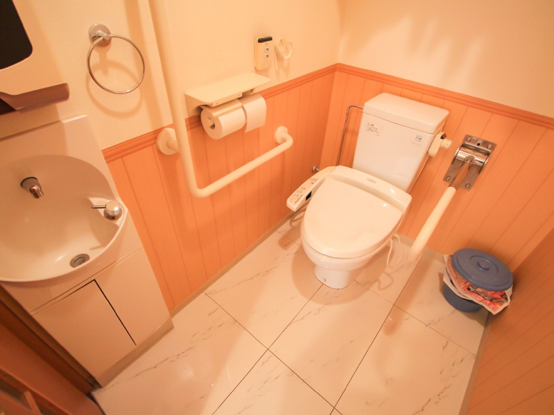 トイレの両側に手すりがつけられていて、移動や立ち座りに便利。洗面台はキャビネットタイプである。広く空間が確保されている。