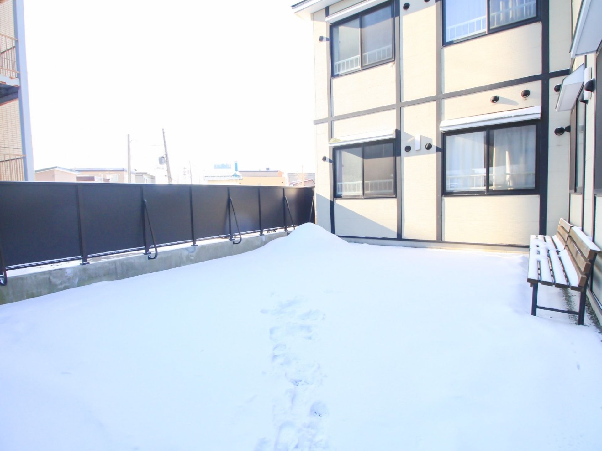 雪が積もっている。ベンチが設置されている。季節によっては散歩などを行える。周囲はフェンスで囲まれている。