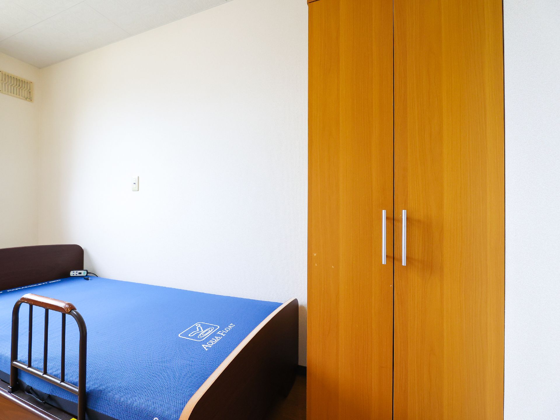 白い壁沿いに青いマットレスのベッドとクローゼットが置かれた部屋