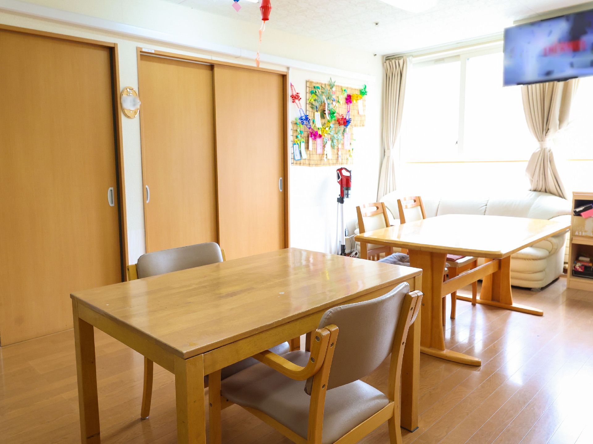ドアが並びテレビが付いた大きな窓と四角いテーブルがある部屋