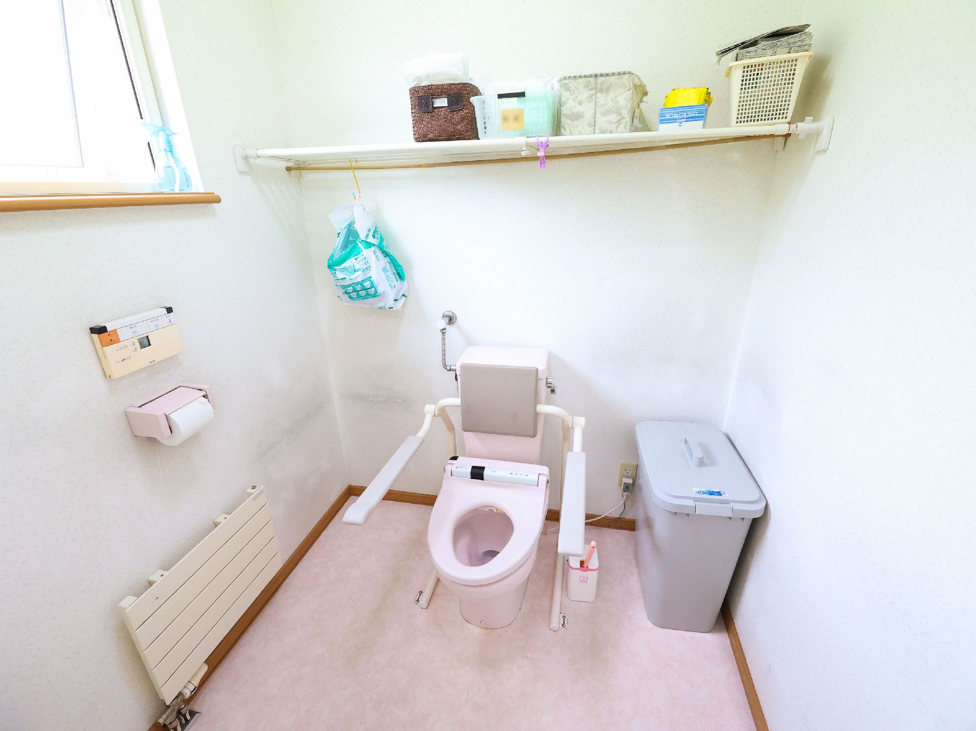 壁沿いにものが飾ってあるピンクの便器と手すりがある四角いトイレ