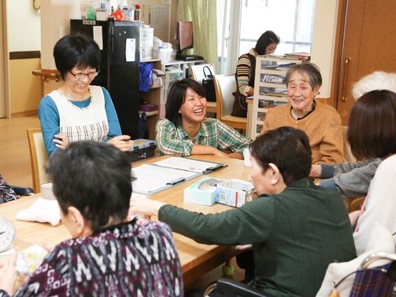 車いすの高齢者もレクリエーションをしているテーブルにつき、一緒に創作活動を楽しんでいる。