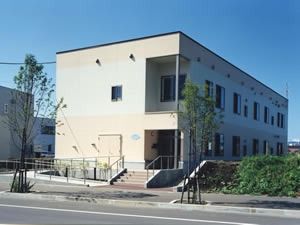 青空の下に建っている２階建ての建物の写真。グループホームの外観写真