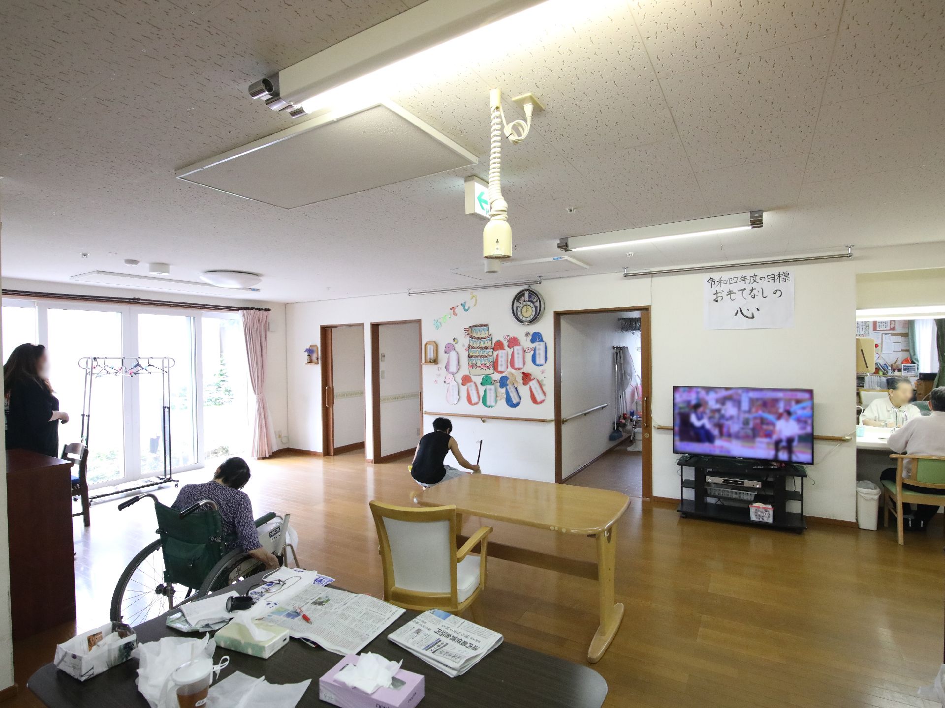 車いすの高齢女性が笑顔でエプロンを付けた若い女性スタッフと手を取り合って話している。