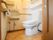 シンプルな洗面台を備えたトイレである。便座の上部に棚を設けている。横側に手すりを設置し、出入口ドアは、スライド式を採用している。