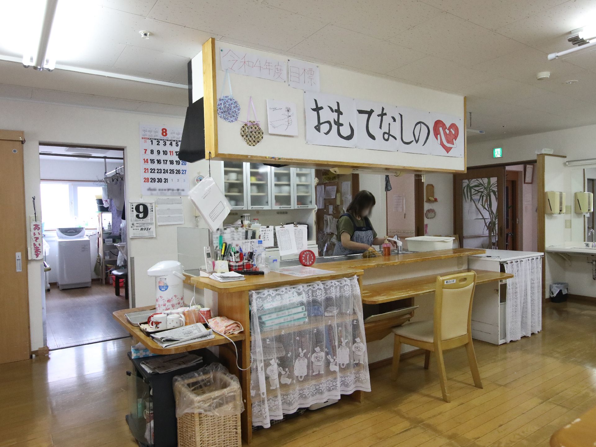 エプロンを付けた若い女性スタッフがフラワーアレンジメントを楽しんでいる眼鏡をかけた高齢男性を手伝っている。