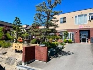 ブルーのポロシャツを着た若い女性スタッフに付き添われて屋外での時間を楽しんでいる車いすの高齢女性。