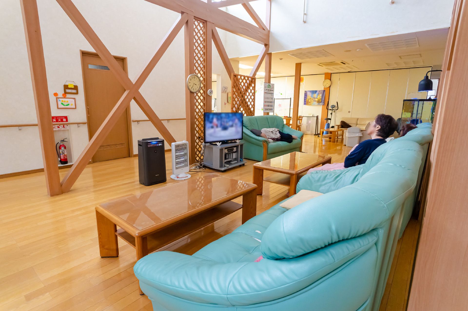 白い壁の広間に置かれたテレビを青いソファーに座ってみている入居者様