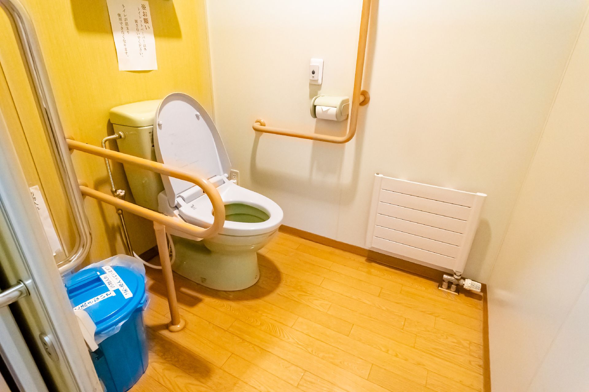 木製の手すりに囲まれた洋式便器がある黄色と白の壁のトイレ