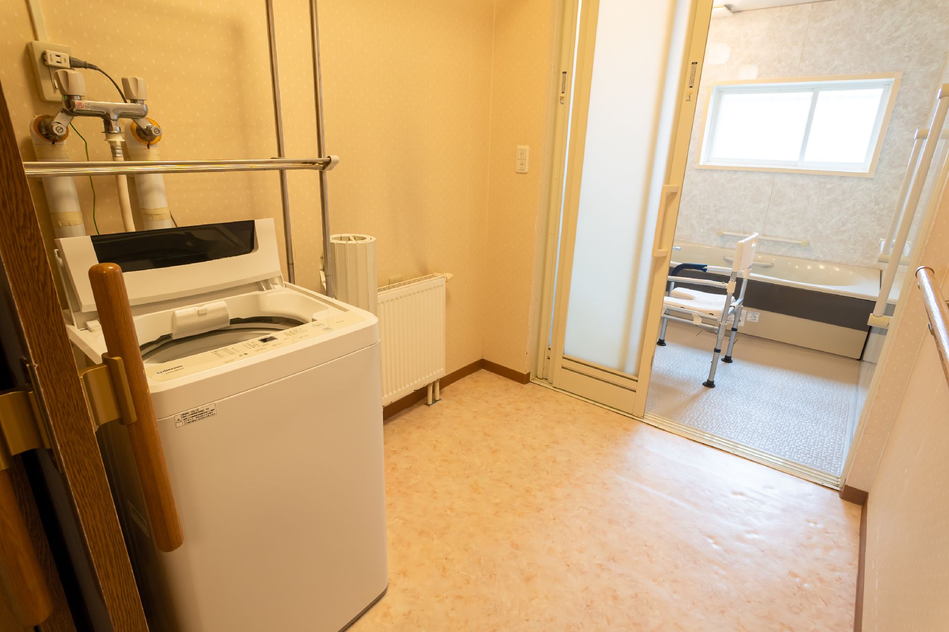 水の入ったコップを持って微笑んでいる若い女性スタッフの前には、薬を飲もうとしている高齢女性がいる。