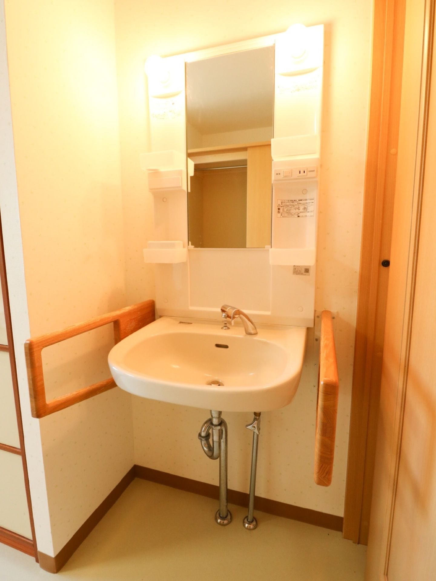 居室の洗面台の左右には手すりがある。専用の照明器具と、歯ブラシなどの日用品を置いていただける棚を備えている。