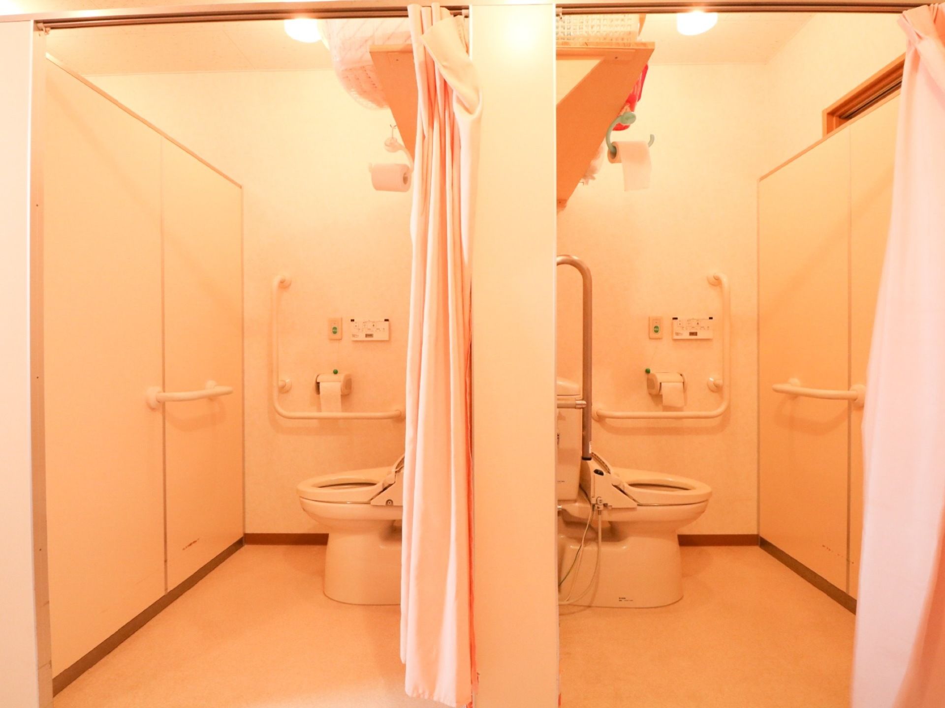 洋式トイレが２ヶ所並んでいる。入り口はカーテンで仕切られている。便器に座って正面の壁にも手すりがある。