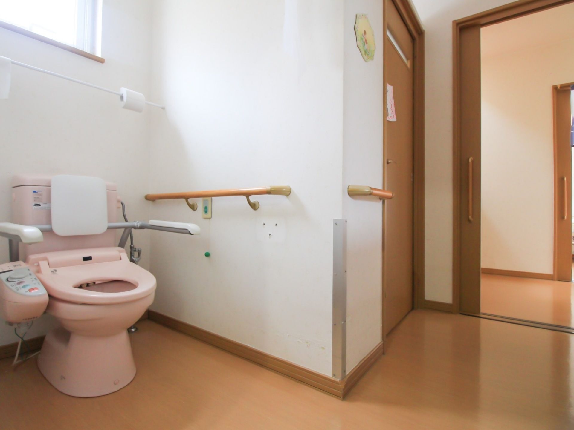 引き戸を開けた所にオープンな造りのトイレがある。便座の周囲に背もたれやひじ掛けが取り付けられている。