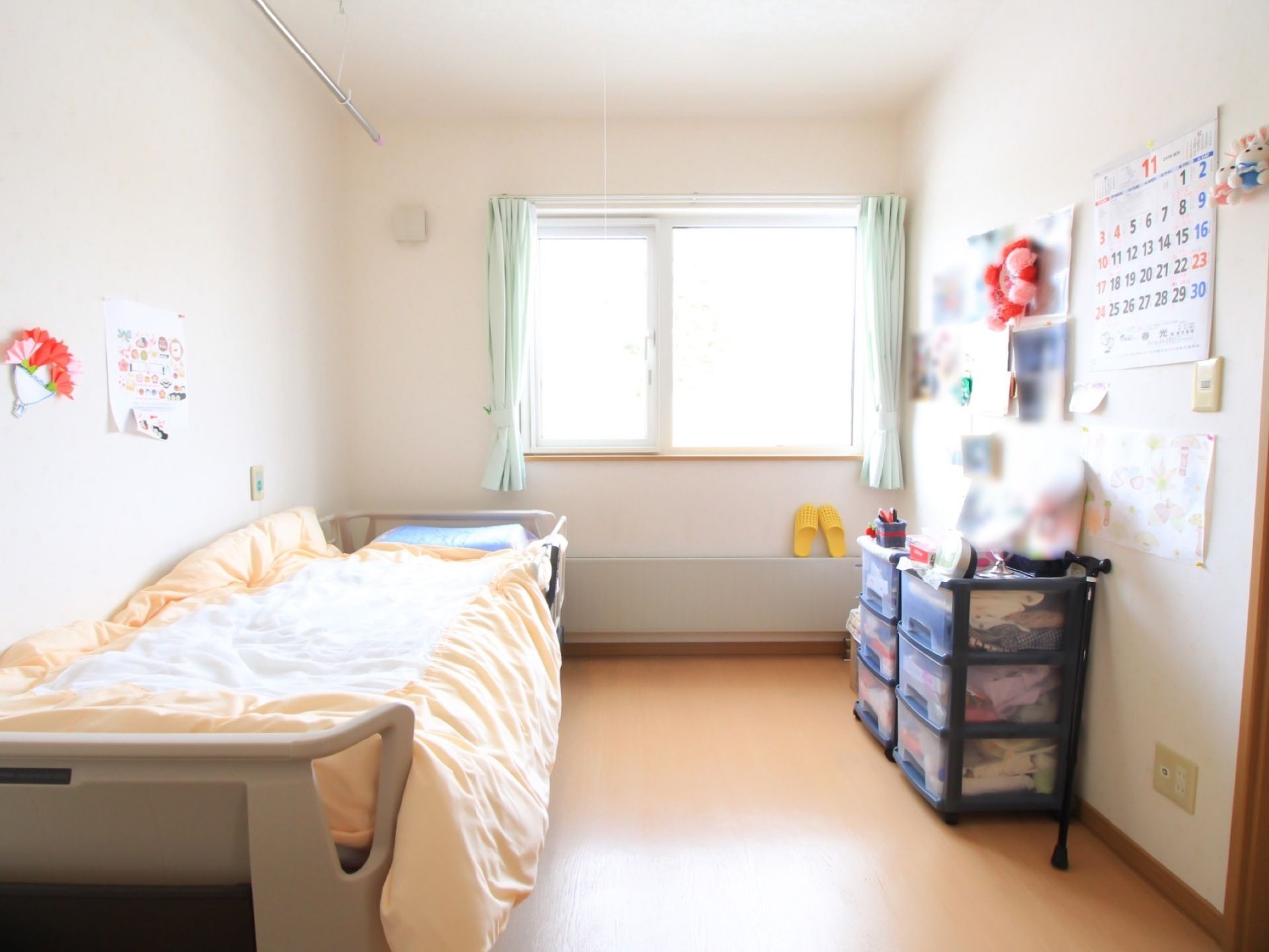 居室には腰高の窓があり、薄い緑色のカーテンがかかっている。窓の下の壁にパネルヒーターが設置されている。