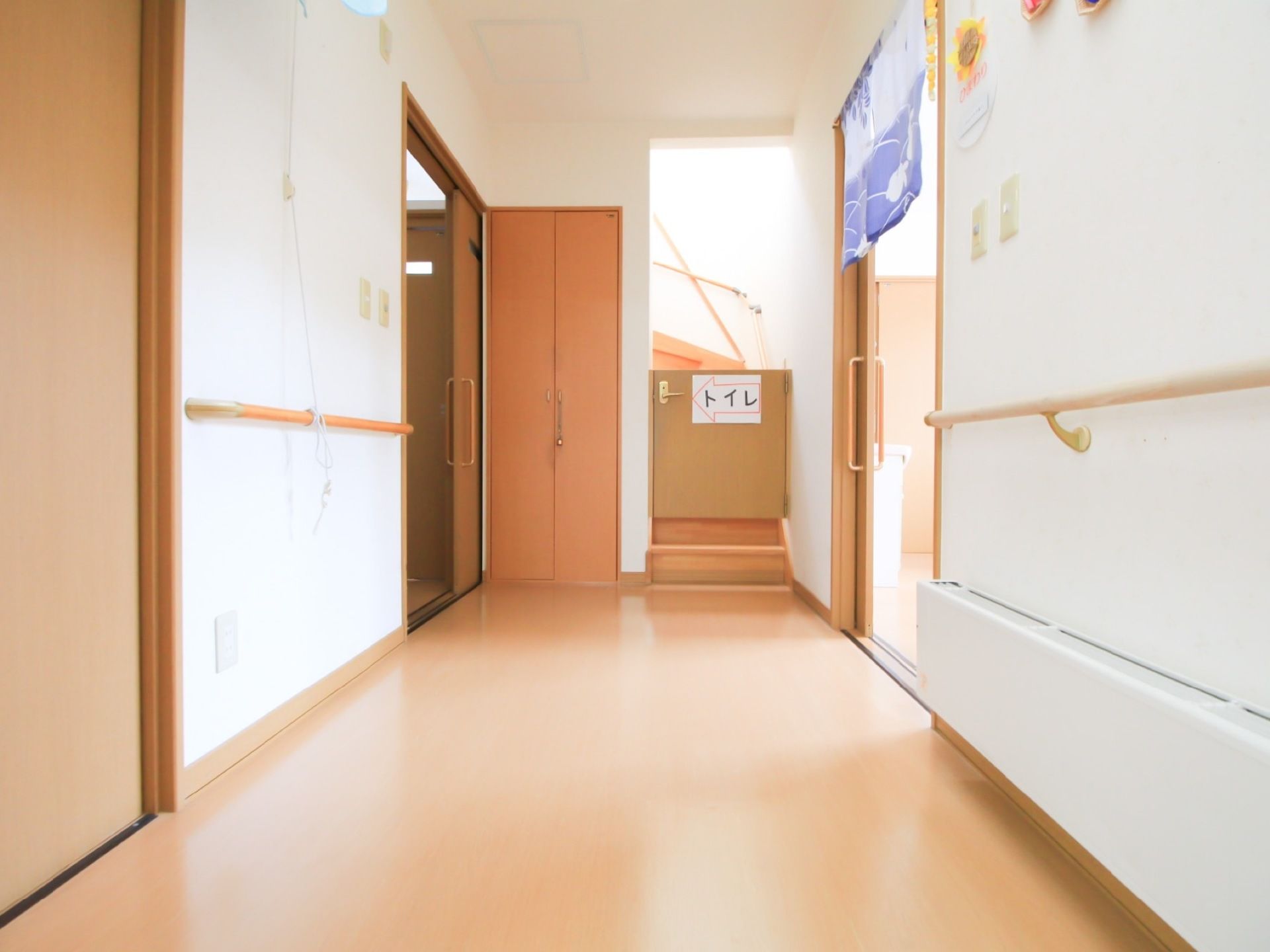 廊下のつきあたりに階段があり、その前にレバーがついた扉が設置されている。トイレの方向を示す表示が貼られている。