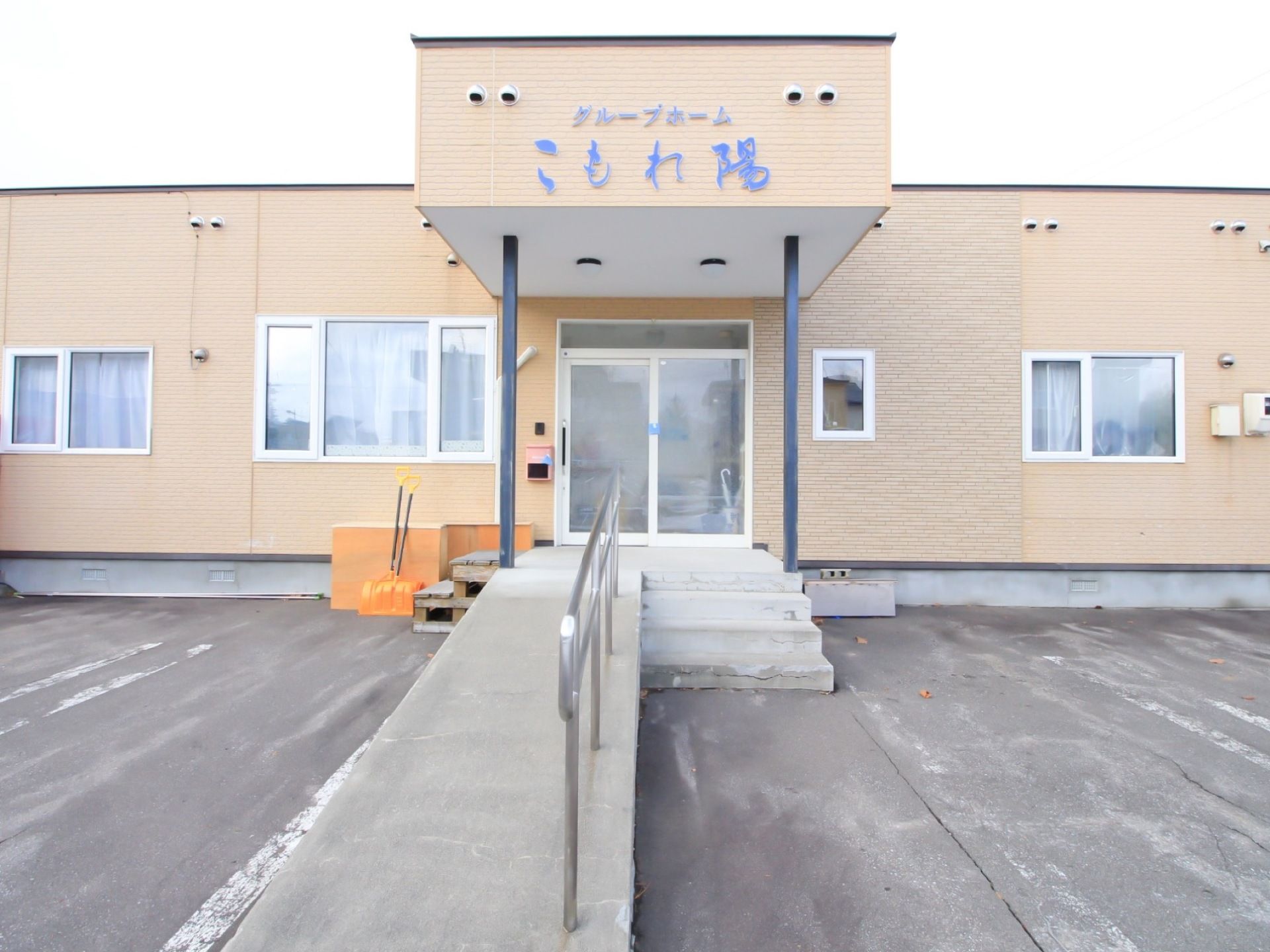 ベージュ色の外壁の平屋建ての施設である。玄関前のひさしの幕板部分に、施設名称が大きく表示されている。