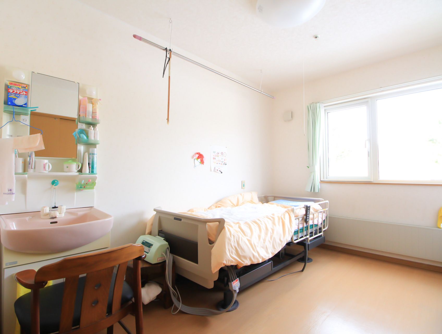 介護用ベッドがあり、洗面台には椅子が置かれている明るい居室