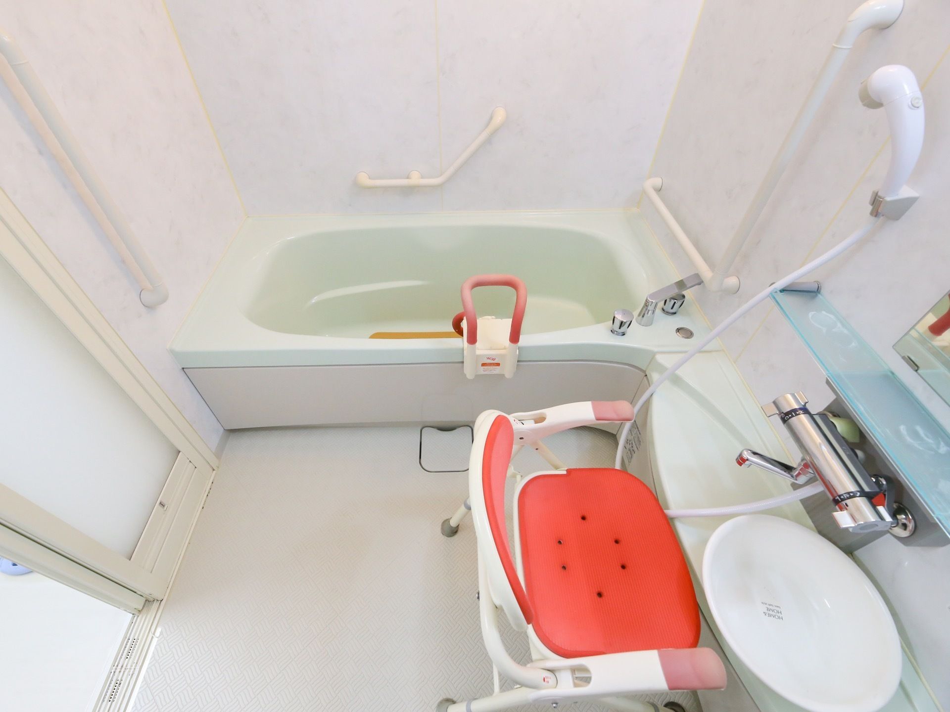 個浴用浴室の一例。奥に浴槽があり、黄色い滑り止めマットが敷かれている。手前は洗い場になっており、左手に入口がある。