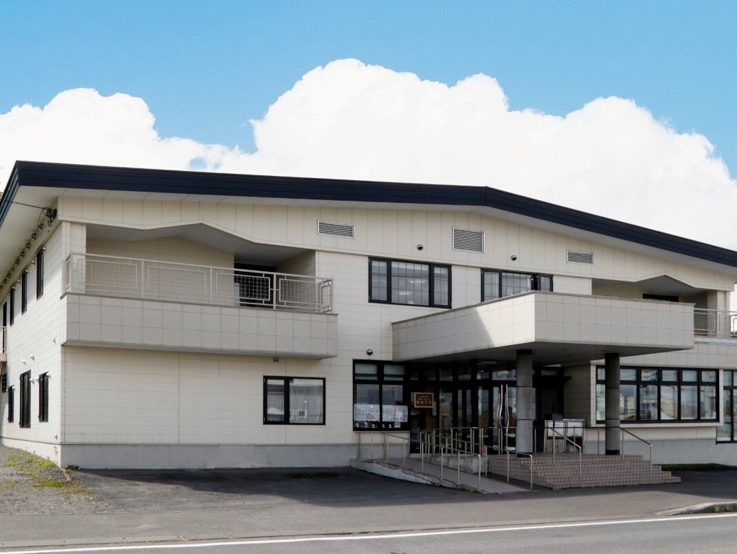 三角屋根が付いた白を基調とした２階建ての建物の玄関には屋根が付き、2階部分にはベランダもある。