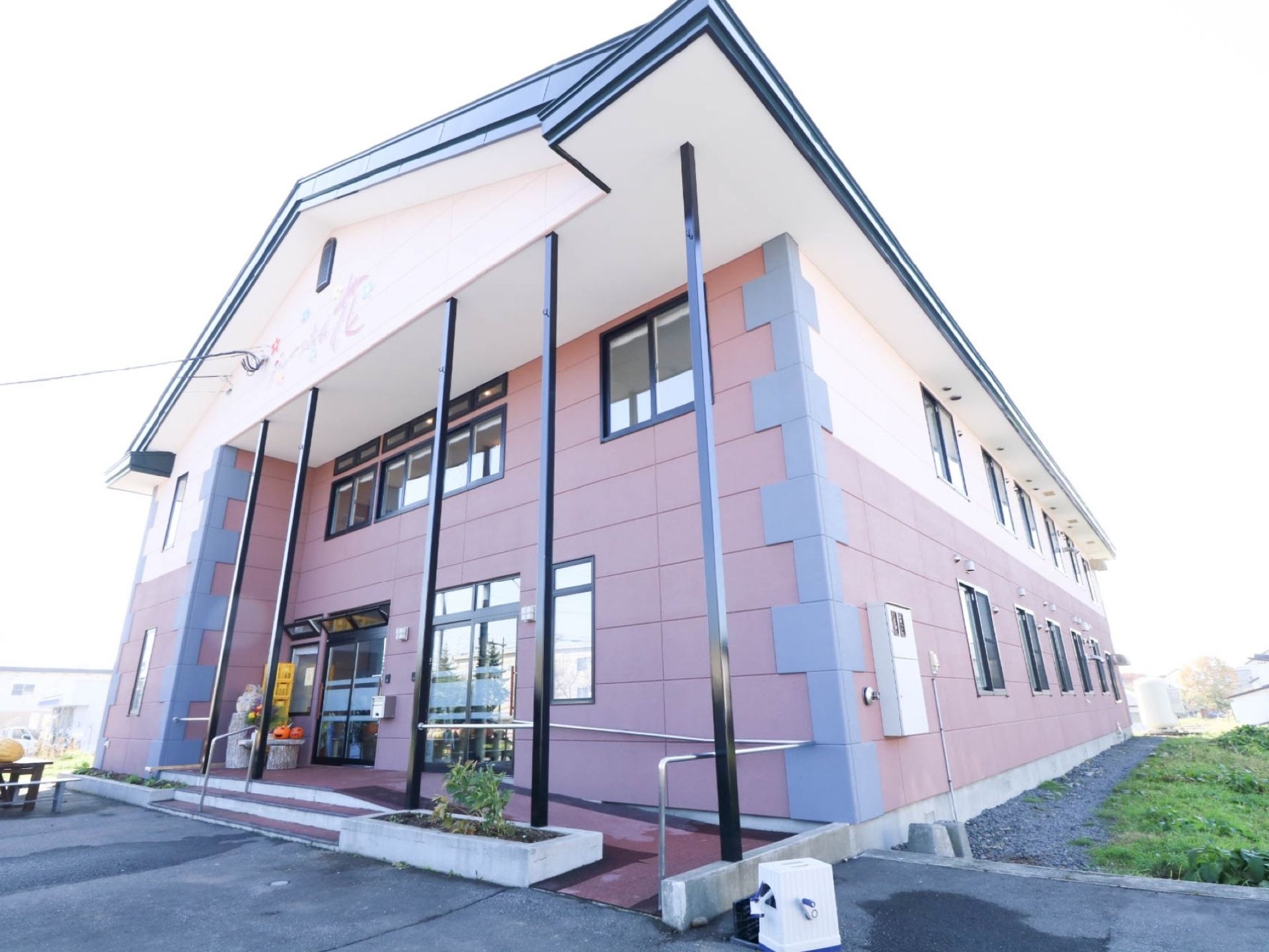 施設の建物はパステルカラーの外壁が、レンガのような模様に作り上げられていて個性的。エントランスのそばには花壇を設けている。