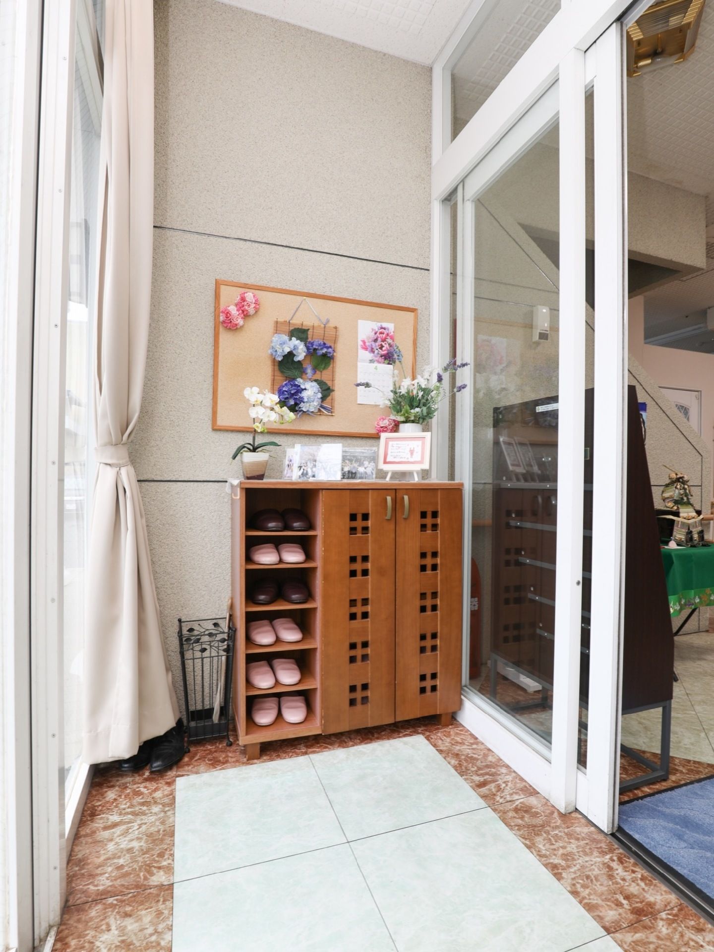扉の付いた靴箱が設置されており、上には花が飾られている。扉はガラス張りになっており、カーテンが取り付けられている。