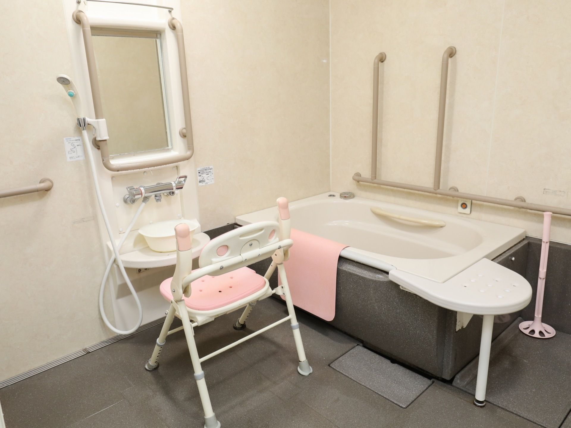洗い場に置かれたシャワーチェアは、背もたれと可動式のひじ掛けが付いている。浴室の壁や浴槽内に手すりが設置されている。