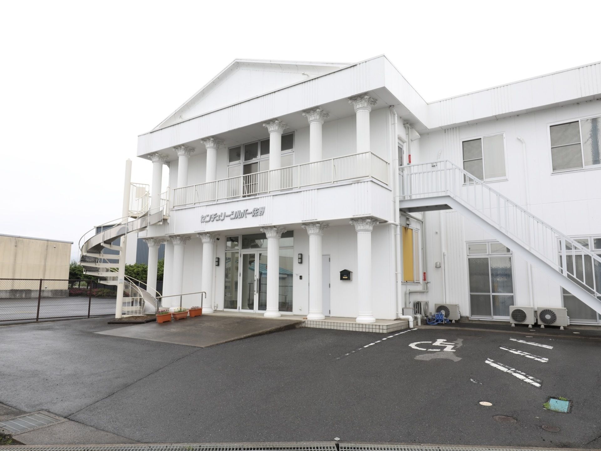 玄関上の外壁に施設名が大きく表示されている。スロープには花が植えられたプランターが３つ並べて置かれている。