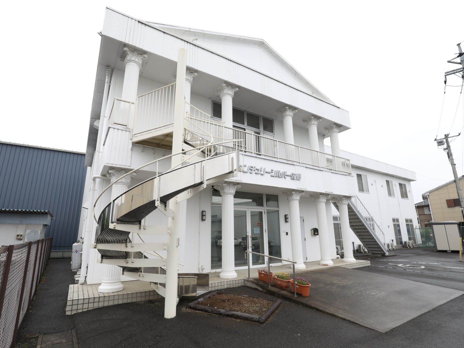 白い２階建ての建物の両サイドに、手すりが付いた階段と緩やかな傾斜の滑り台が設置されており、下に砂場がある。