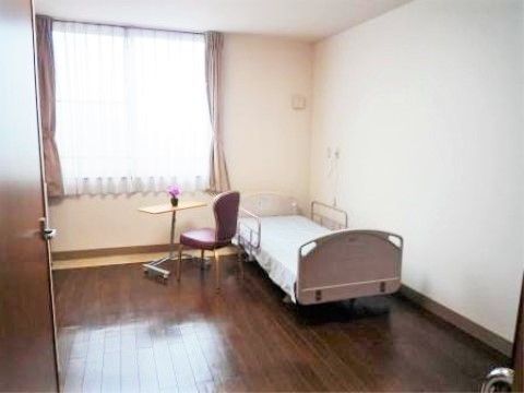 明るい日が差し込む部屋に、ベッドとテーブルセットが置かれている居室